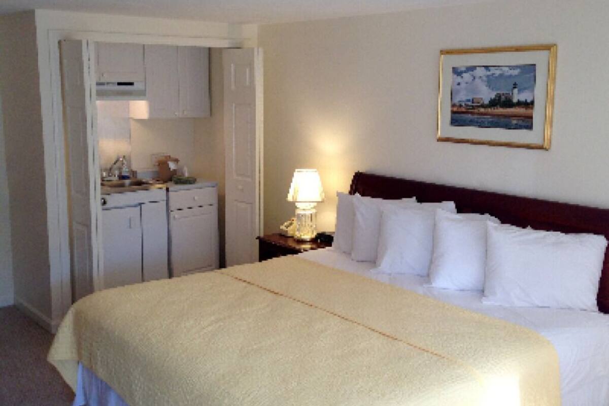 Une chambre d’hôtel avec un lit, une table de chevet avec une lampe, un tableau au mur et un coin cuisine.