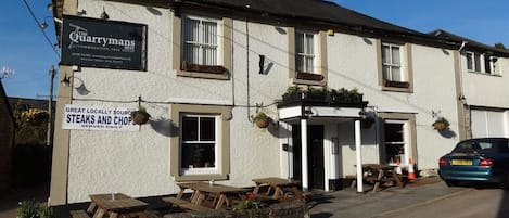 A building with a sign for 'The Quarrymans' accommodation and free house, featuring outdoor seating and a stone wall.