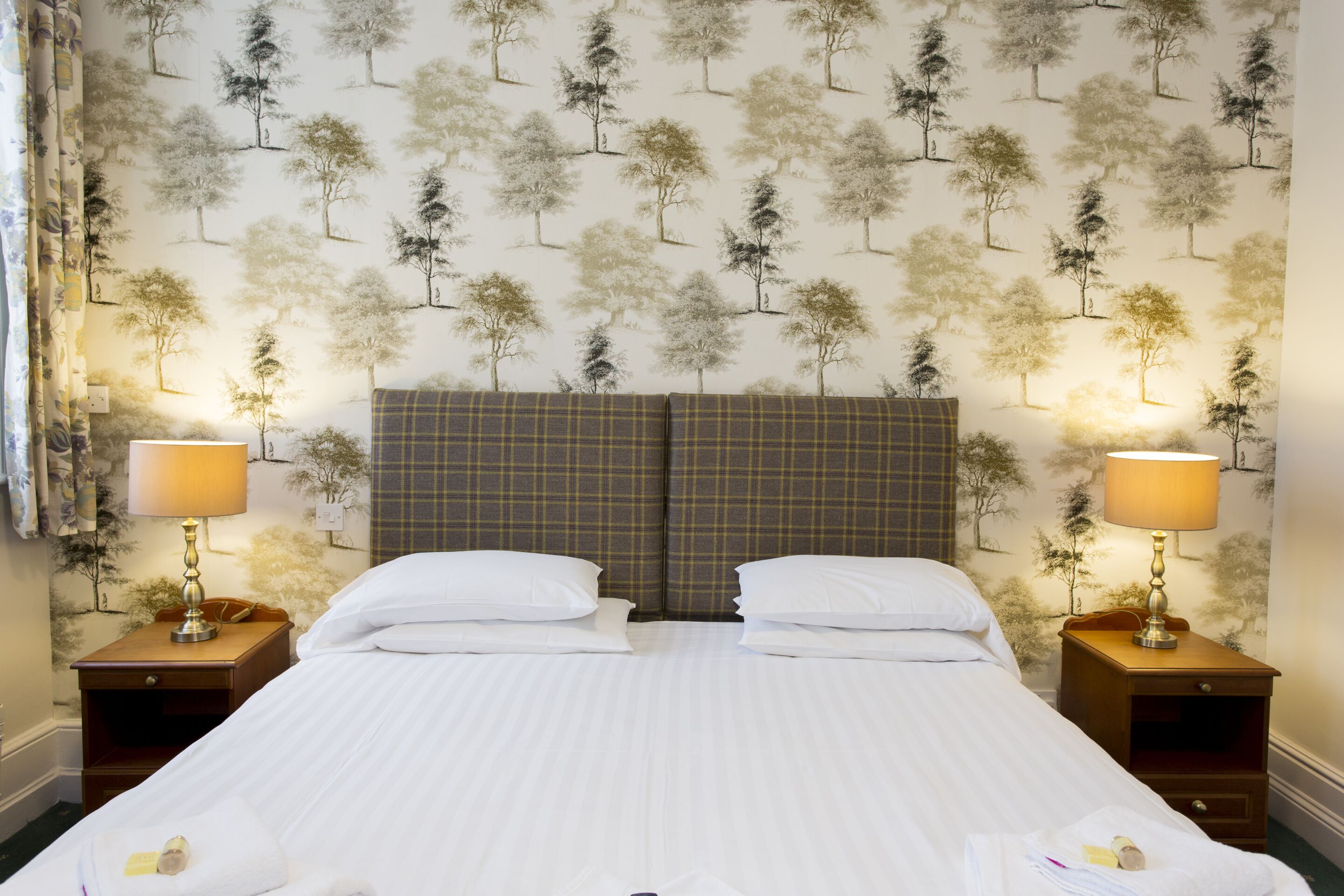 A neatly made bed with white linens, two bedside tables with lamps, and a wall with a tree pattern.