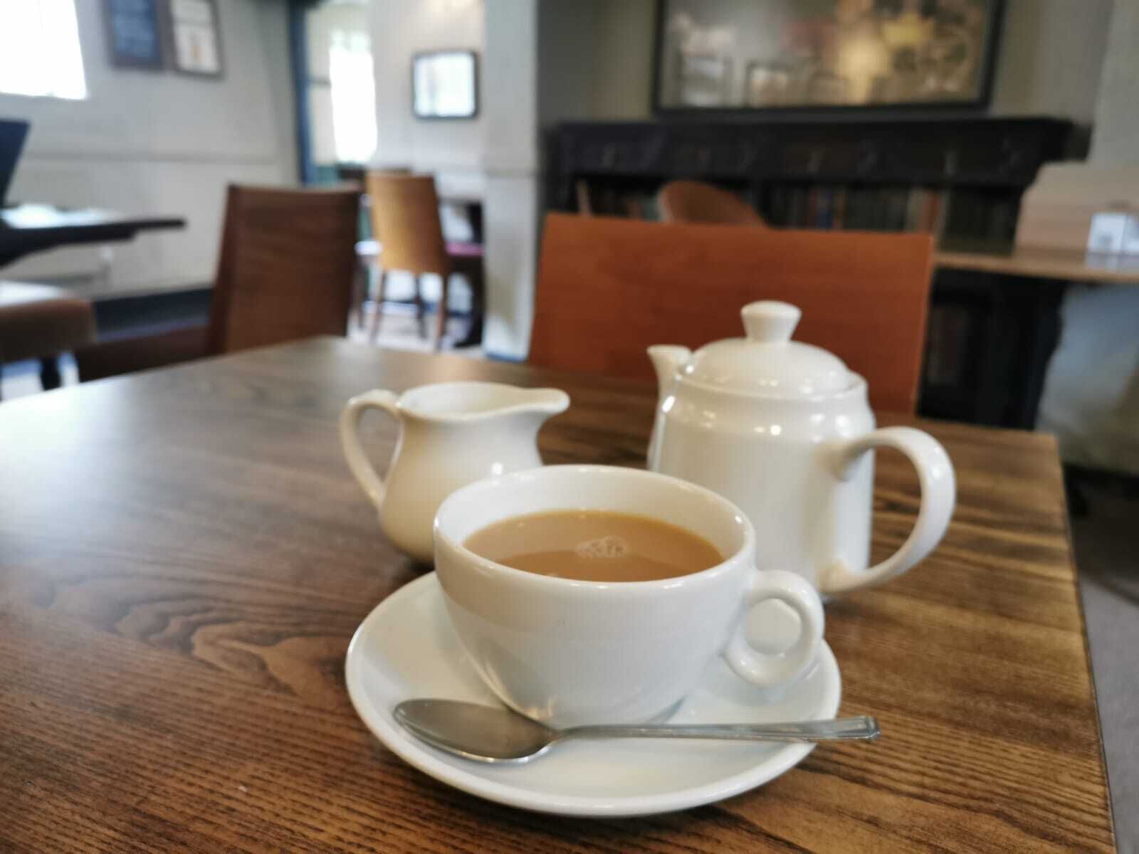 Una mesa de madera con una tetera blanca, una taza blanca y un platillo con una cuchara.