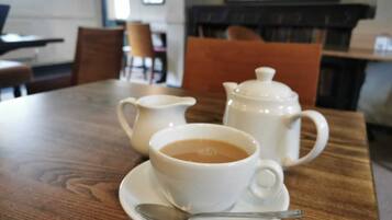 Una mesa de madera con una tetera blanca, una taza blanca y un platillo con una cuchara.