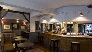 A bar area with wooden stools, a counter with bottles, and framed pictures on the wall. - The Old Bell Inn (Warminster)