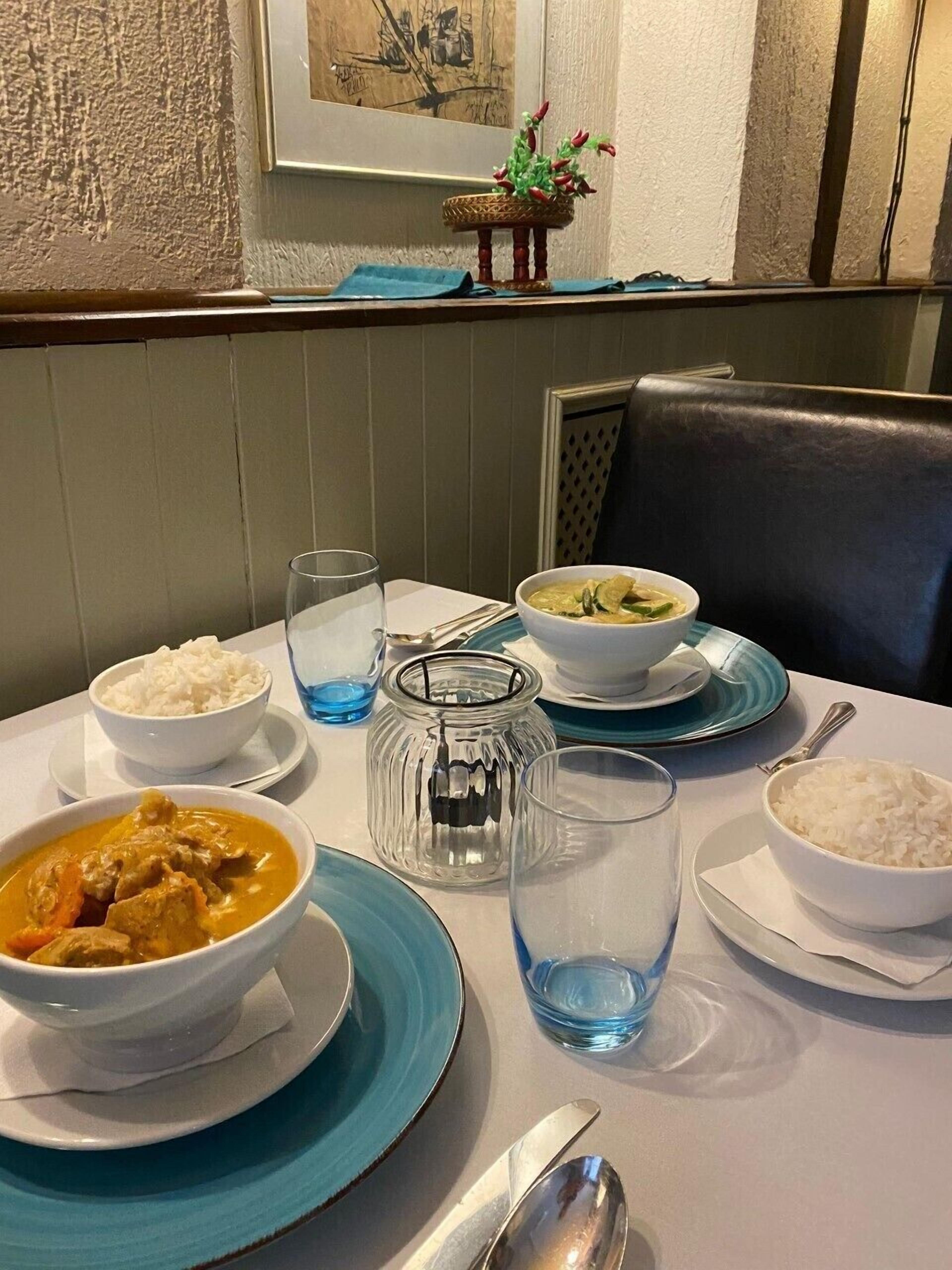 Ein Esstisch, gedeckt mit Schüsseln Reis, Curry und Suppe, dazu ein Kerzenhalter und eine Vase mit Blumen.