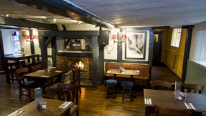 A restaurant with wooden tables and chairs, a bar area, and a fireplace. - The Old Bell Inn (Warminster)