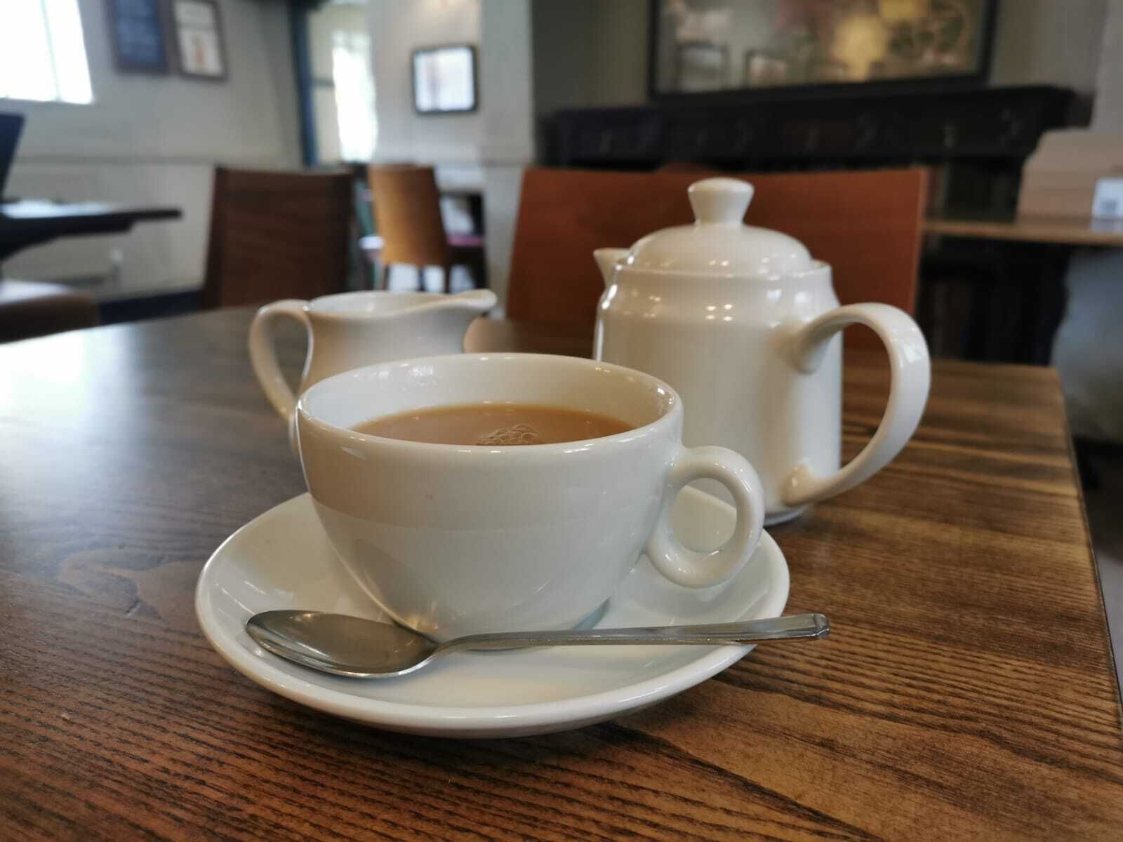 Une table avec une tasse et une soucoupe à café blanches, une cuillère et une théière blanche.