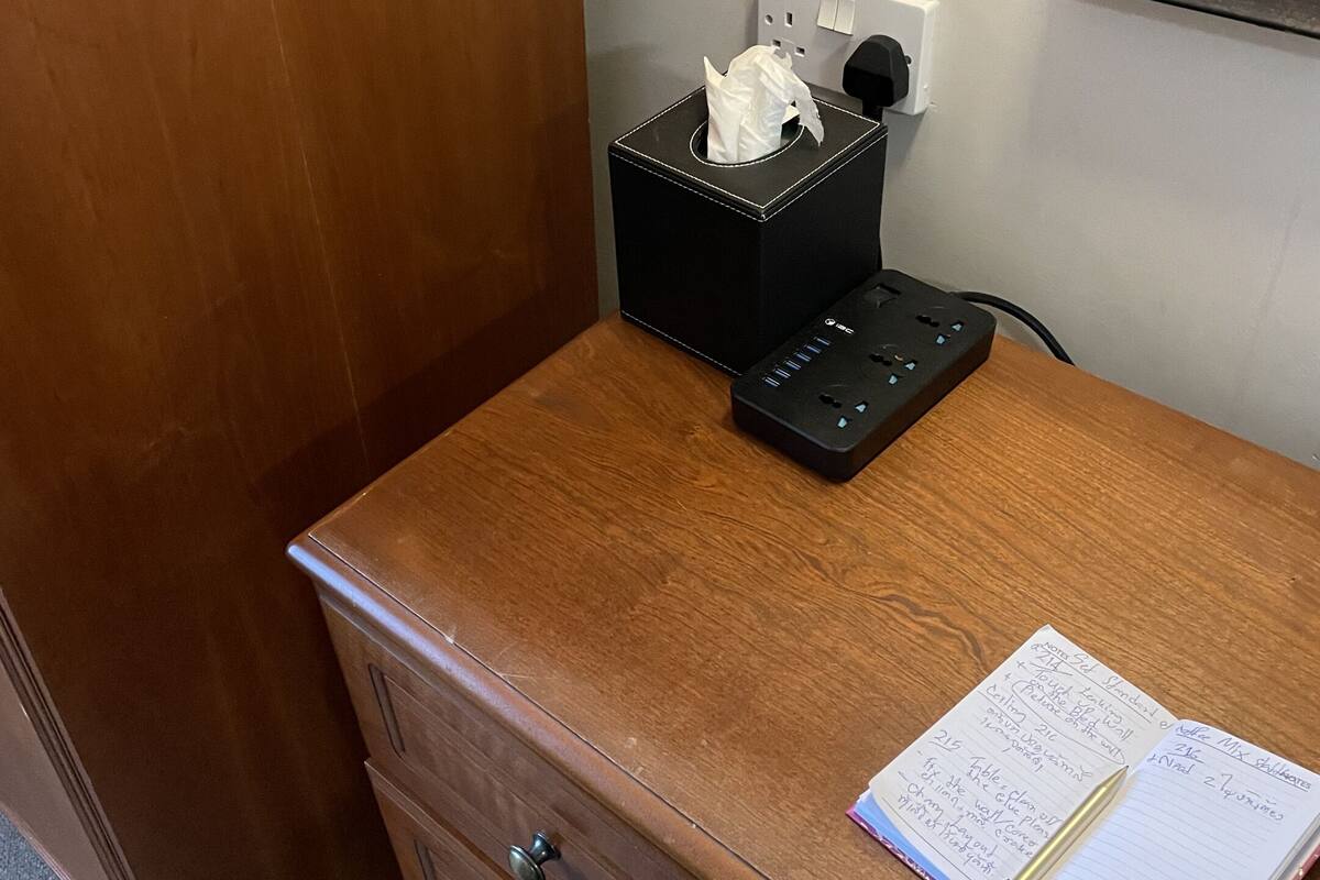 A wooden desk with a black tissue box, a power strip, and a notebook with a pen.