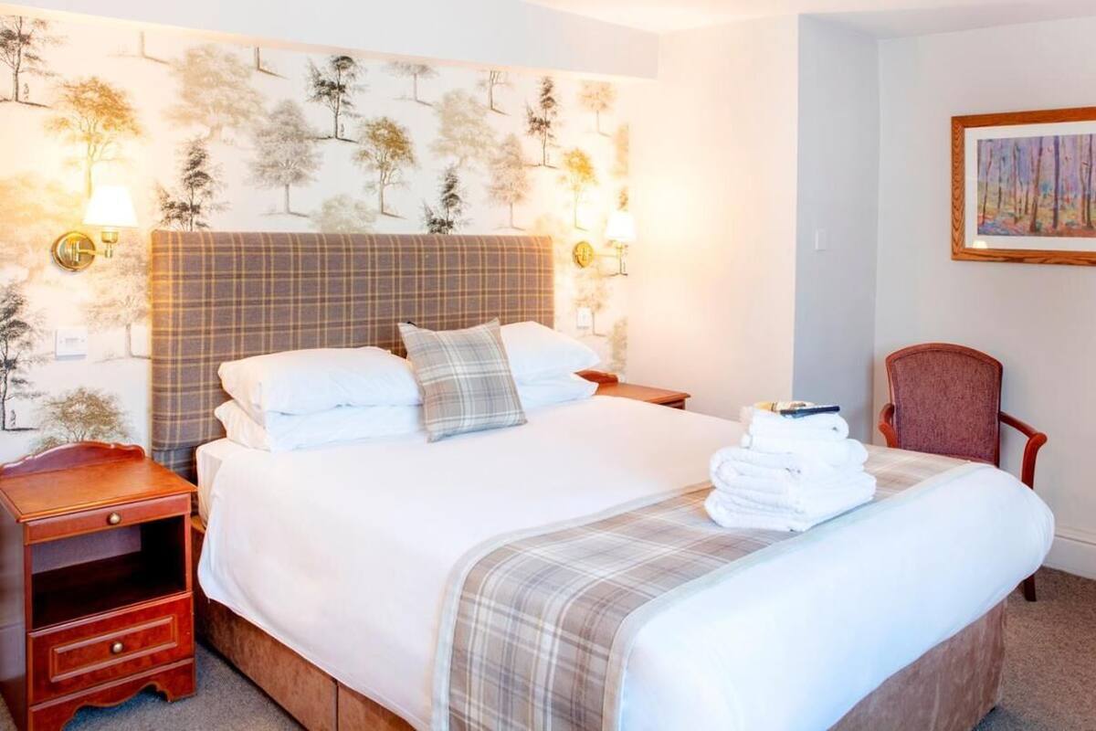 A neatly made bed with a plaid headboard, a bedside table with a lamp, and a chair.