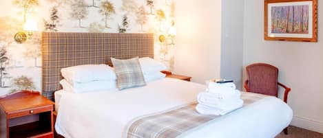 A neatly made bed with a plaid headboard, a bedside table with a lamp, and a chair.