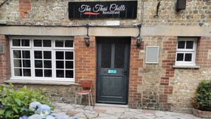 A brick building with a sign reading "The Thai Chilli Restaurant." There is a fire exit door, a chair outside, and a stone-paved entrance. - The Old Bell Inn (Warminster)