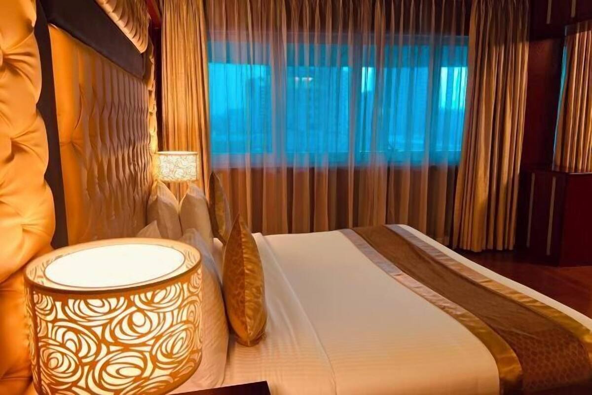 A hotel room with a bed, a lamp, curtains, and a view through the window.