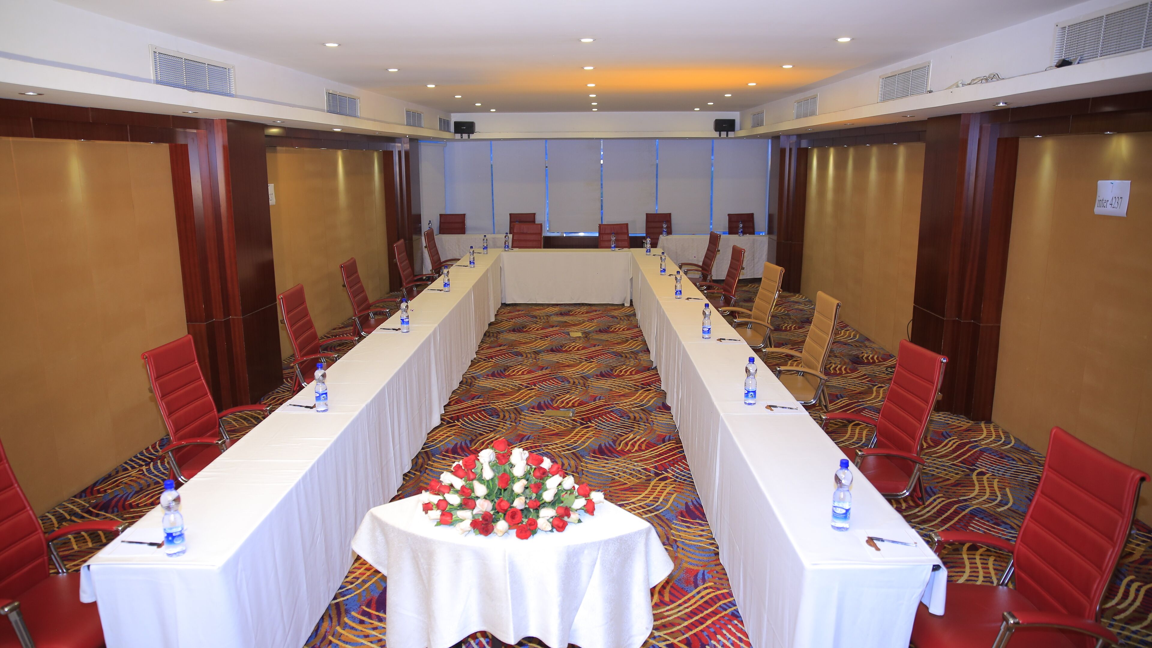 Une salle de conférence avec une longue table, des chaises rouges et un arrangement floral au centre.