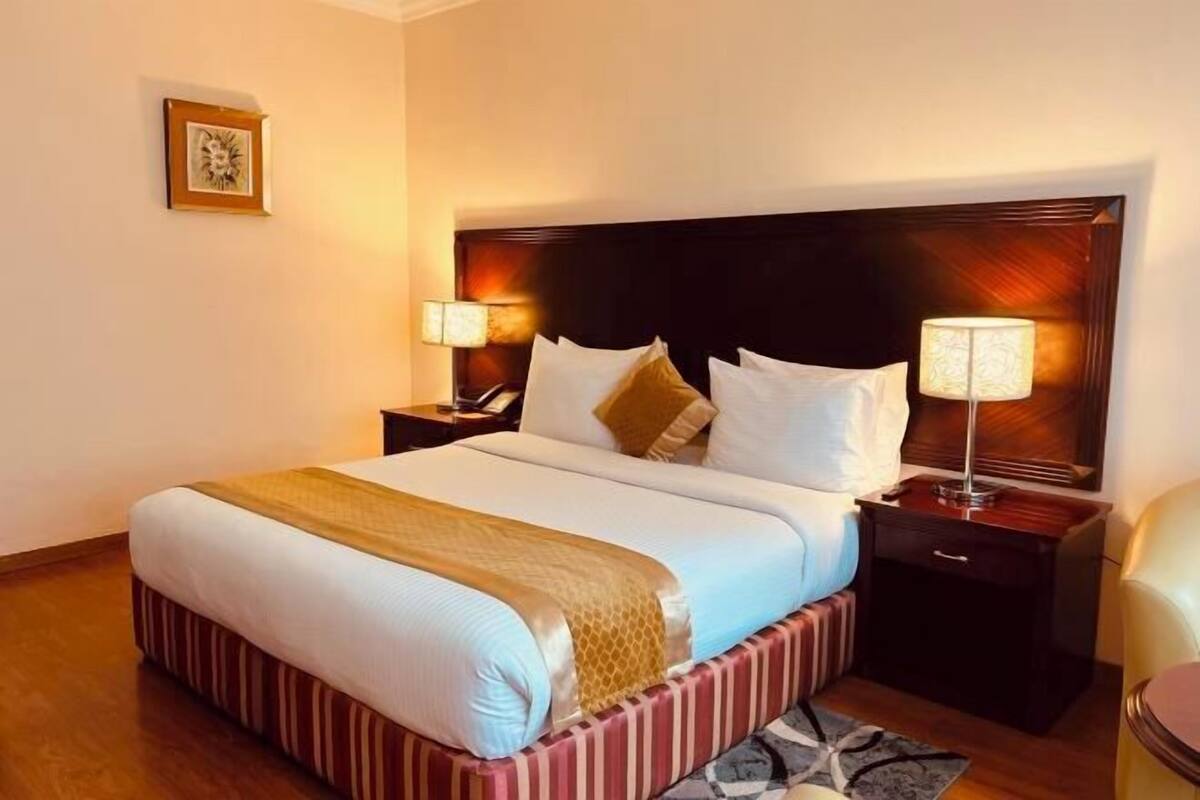 A hotel room with a large bed, two bedside tables, a headboard, and a framed picture on the wall.