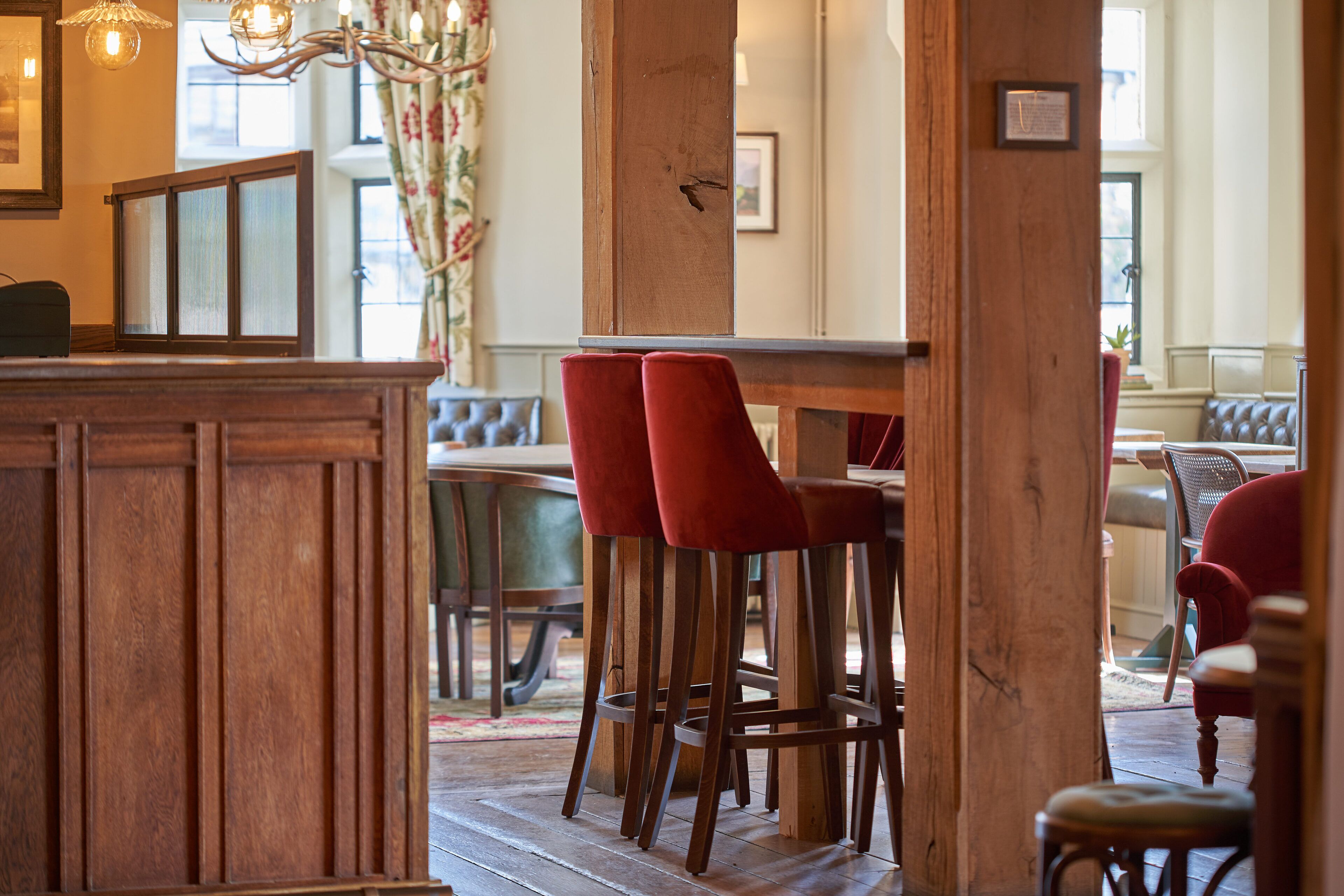 Una zona de bar con barra de madera, sillas tapizadas en rojo y un banco de madera.