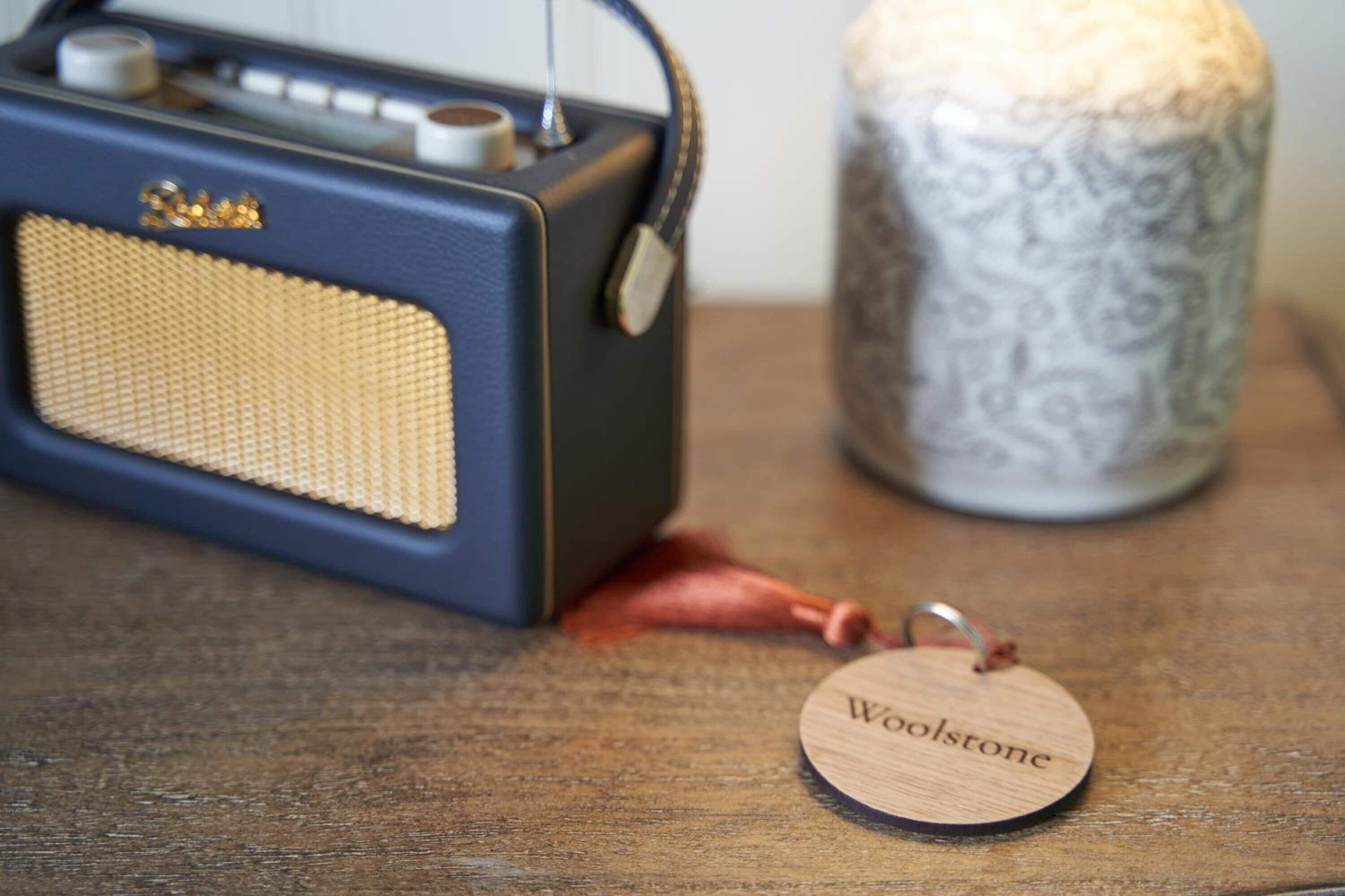A vintage radio, a decorative vase, and a wooden tag on a wooden surface.