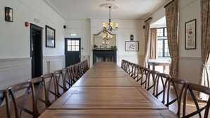 Une longue table en bois, des chaises, un lustre et des œuvres d’art encadrées accrochées aux murs.