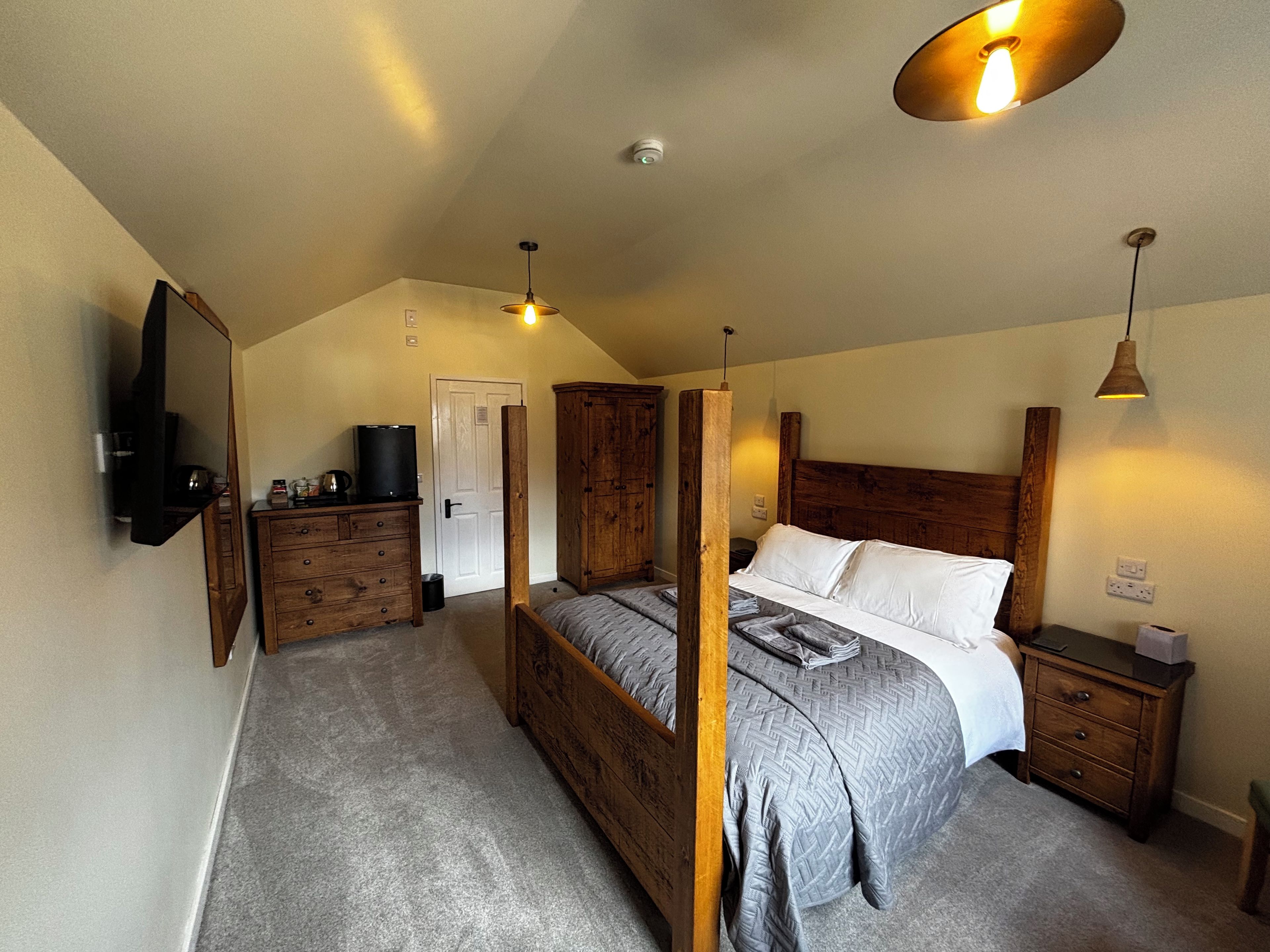 A bedroom with a four-poster bed, wooden wardrobe, bedside table, and a mounted television.
