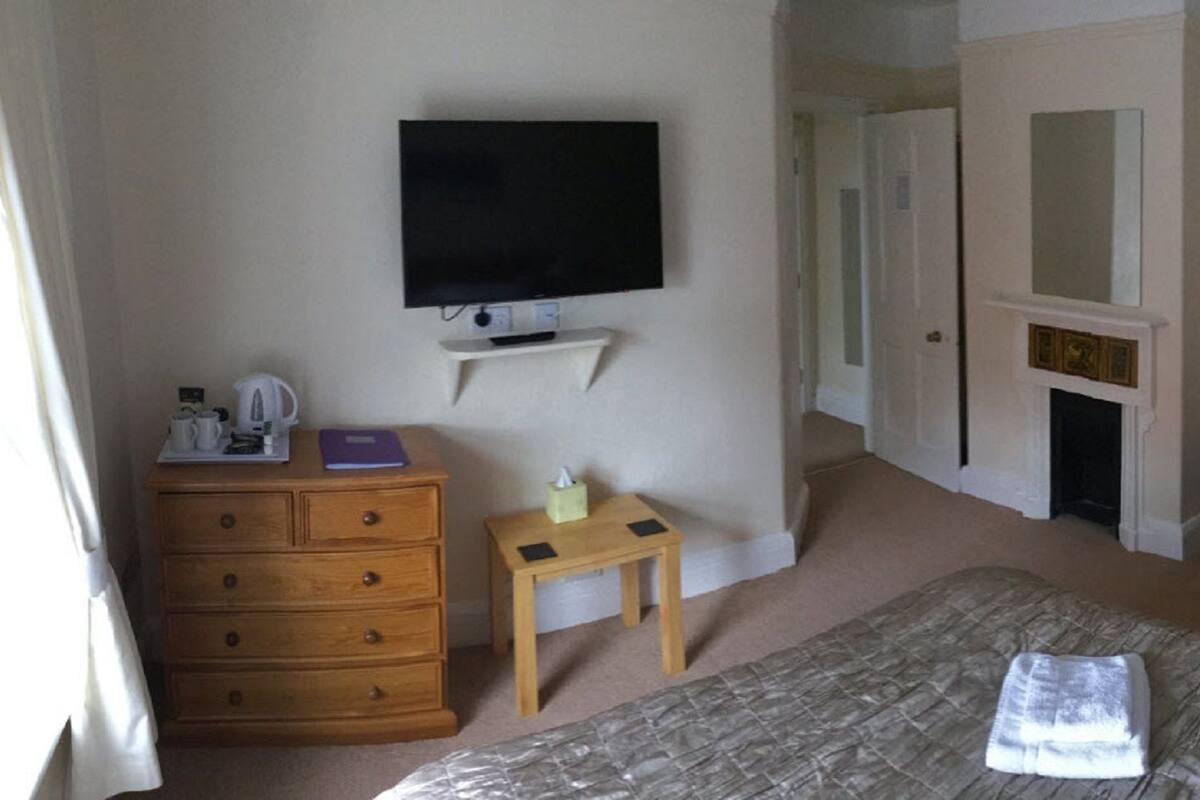 Una habitación de hotel con una cama, televisión, armario de madera, una silla, una mesita y chimenea.