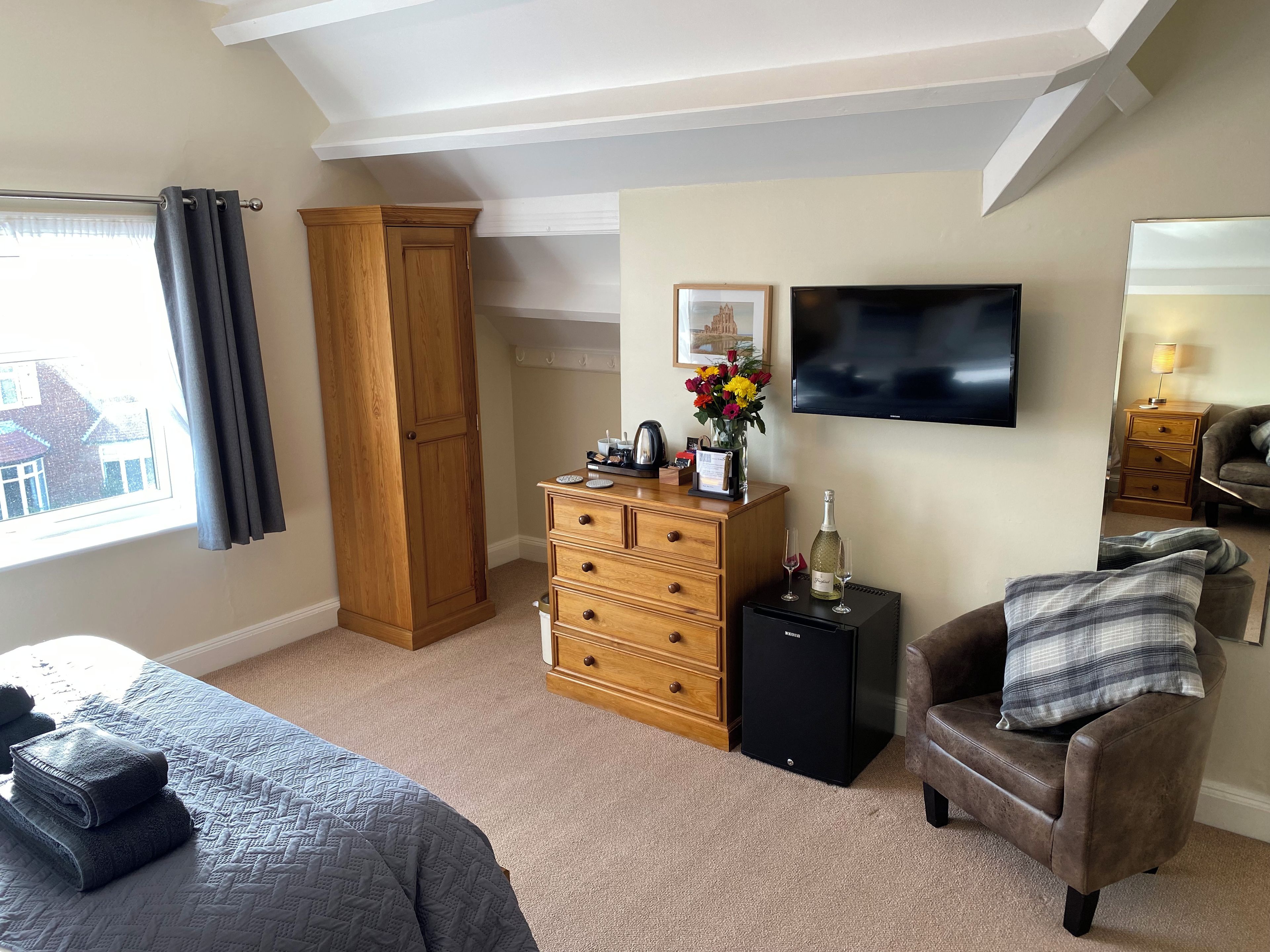 A hotel room with a bed, a wooden wardrobe, a dresser, a television, and a window with curtains.