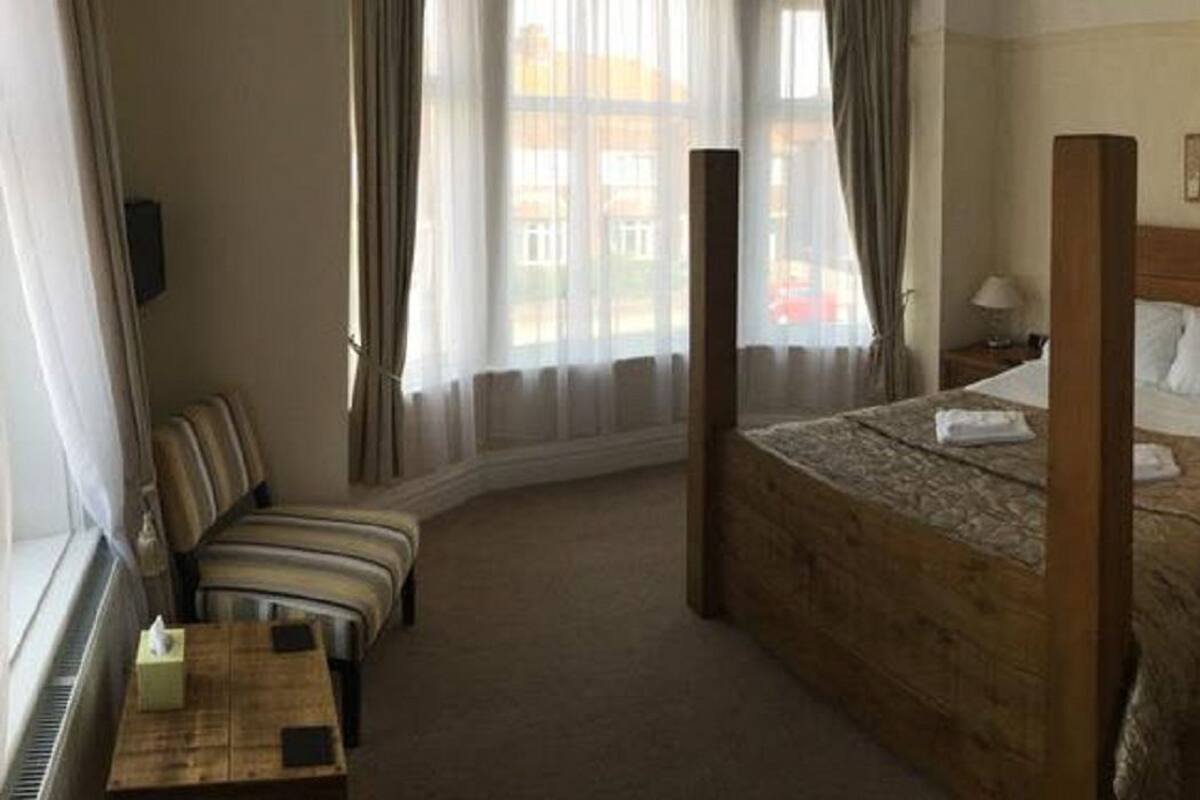 Habitación de hotel con cama con dosel, un área de descanso con sofá y sillones, una mesita con juego de té y vistas a la ciudad a través de amplias ventanas.