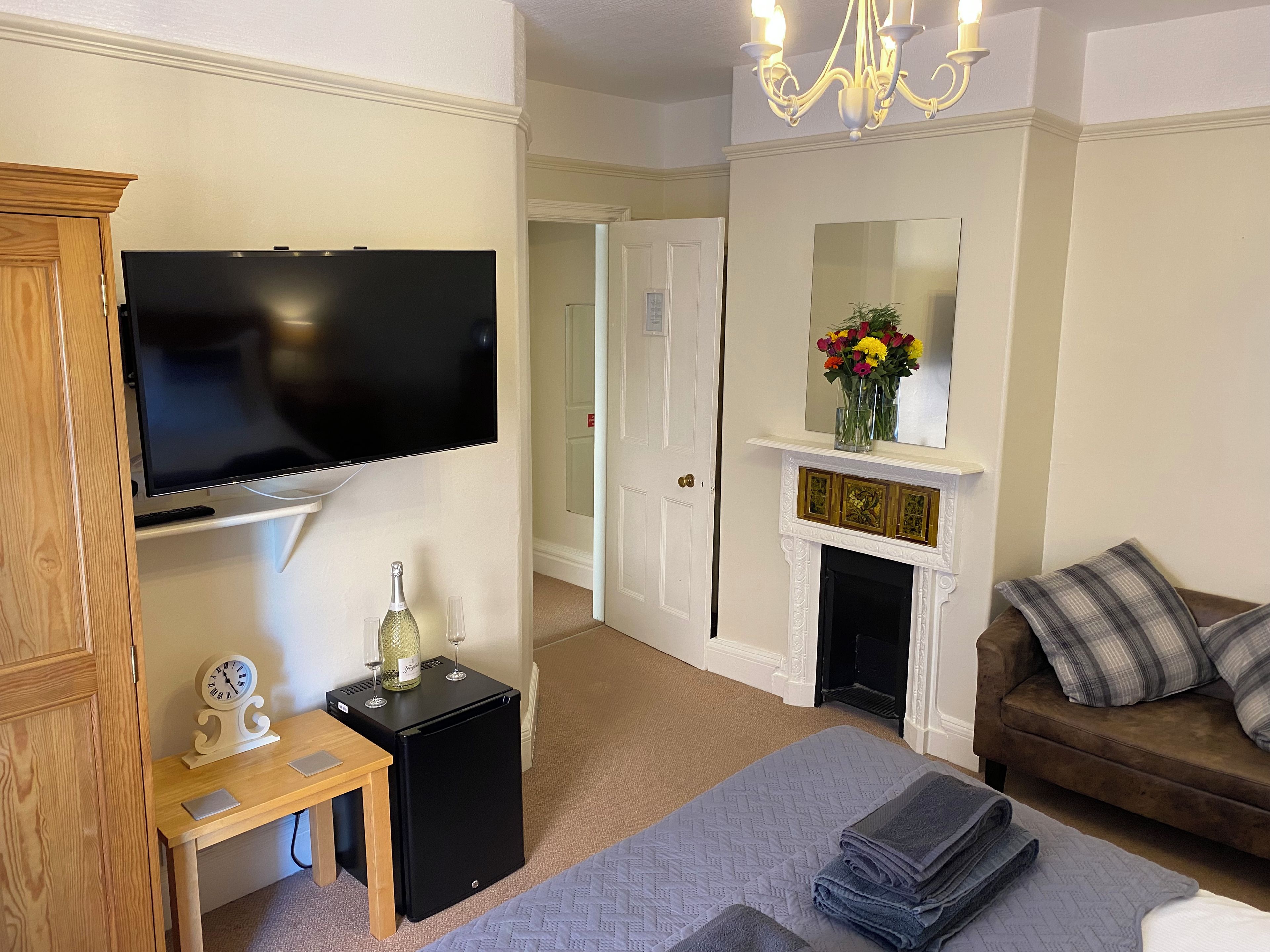 A living room with a flat-screen TV, a small table with a clock, a fireplace, and a sofa.