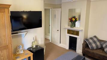 A living room with a flat-screen TV, a small table with a clock, a fireplace, and a sofa.