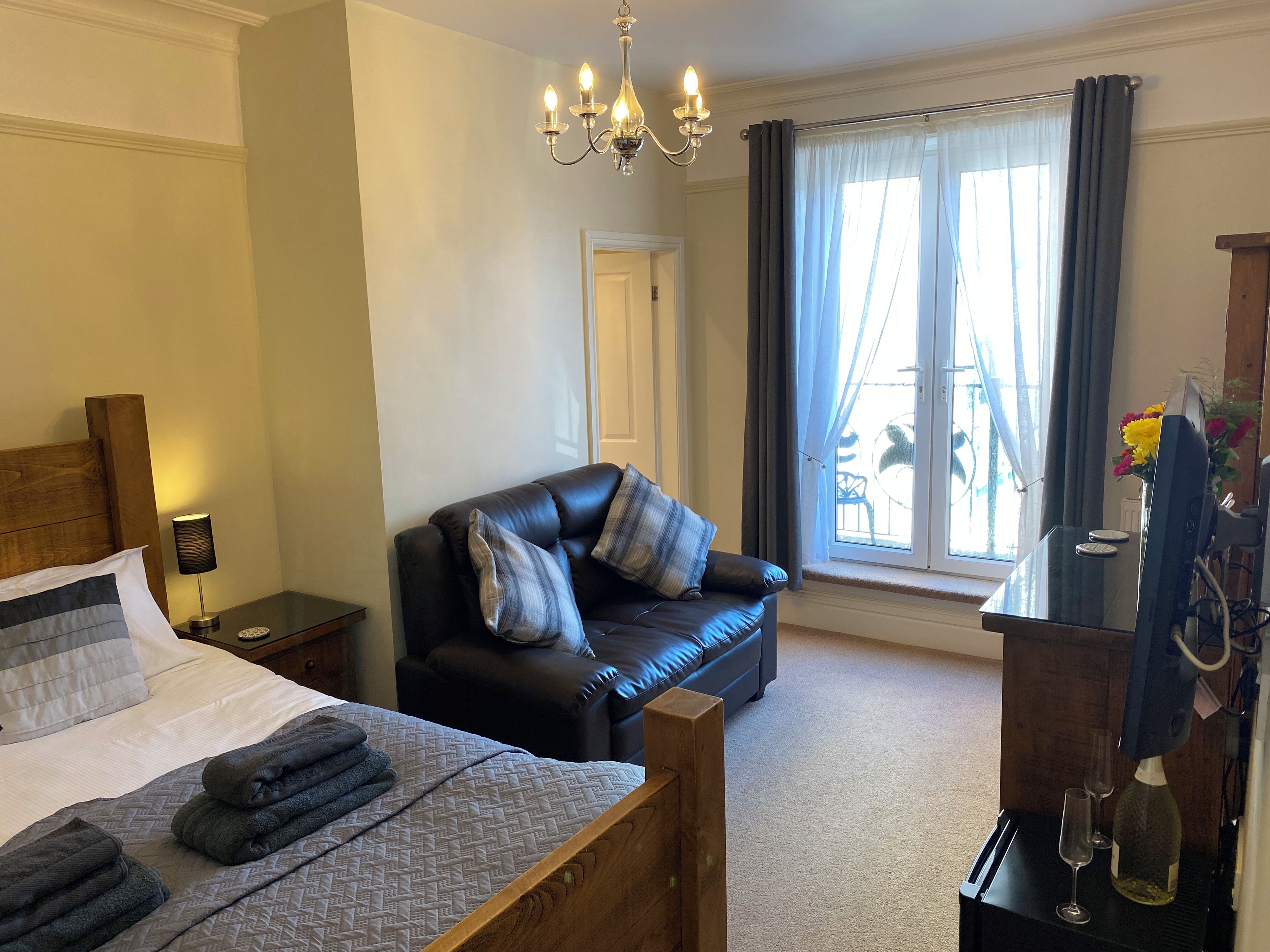 A bedroom with a bed, a sofa, a desk with a computer, and a window with curtains.