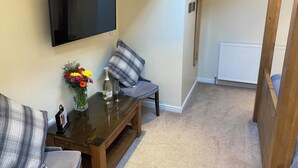 Een woonkamer met een flatscreen televisie, een salontafel met een bloevas, een grijze bank en een houten bankje.