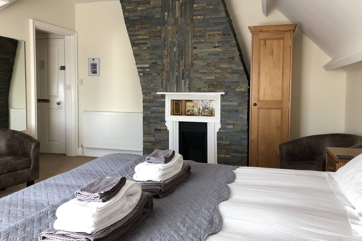 Un dormitorio con techo inclinado, chimenea, armario de madera y cama con toallas dobladas.