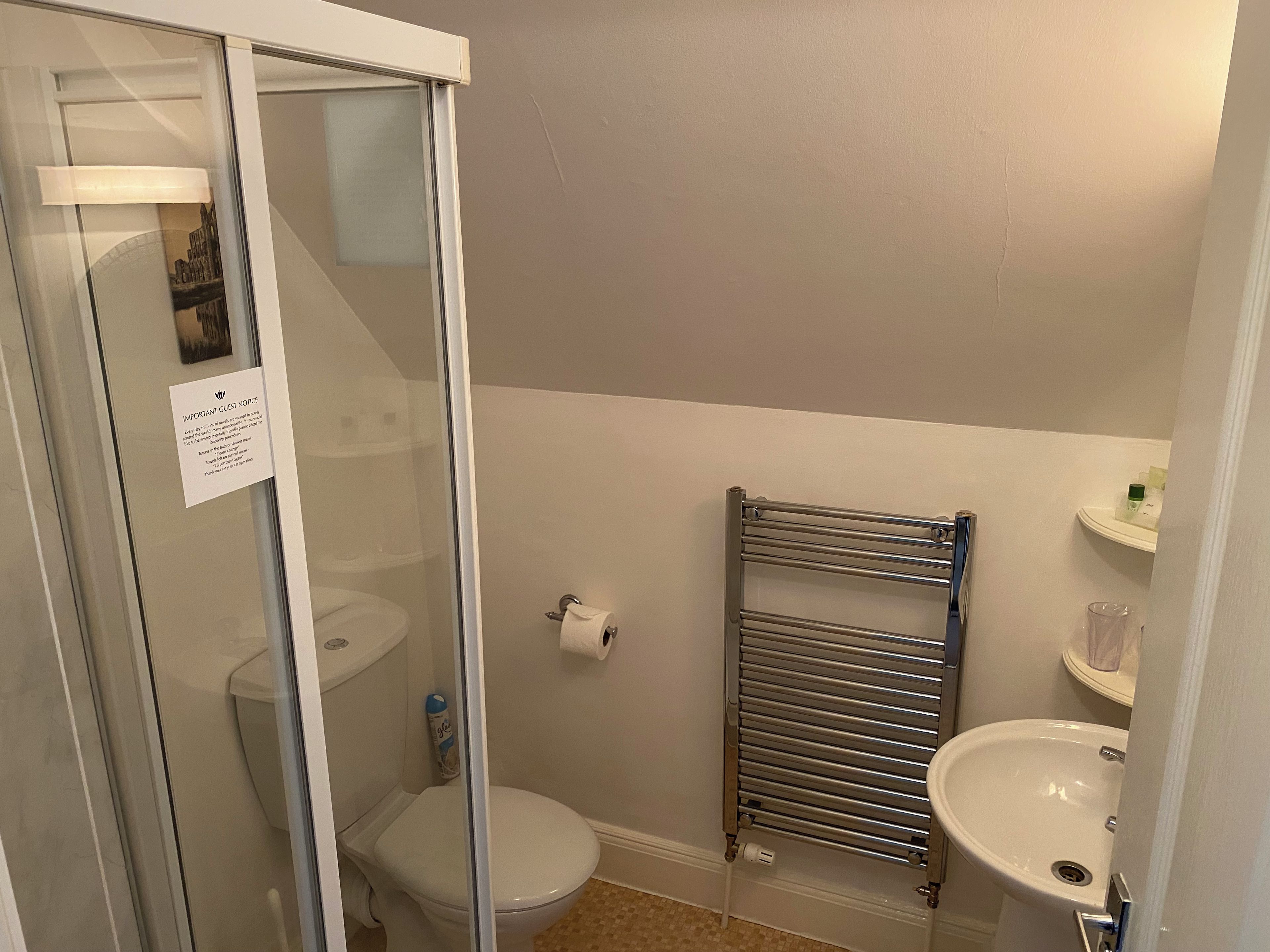 A bathroom with a toilet, a sink, a towel rack, and a glass shower enclosure.