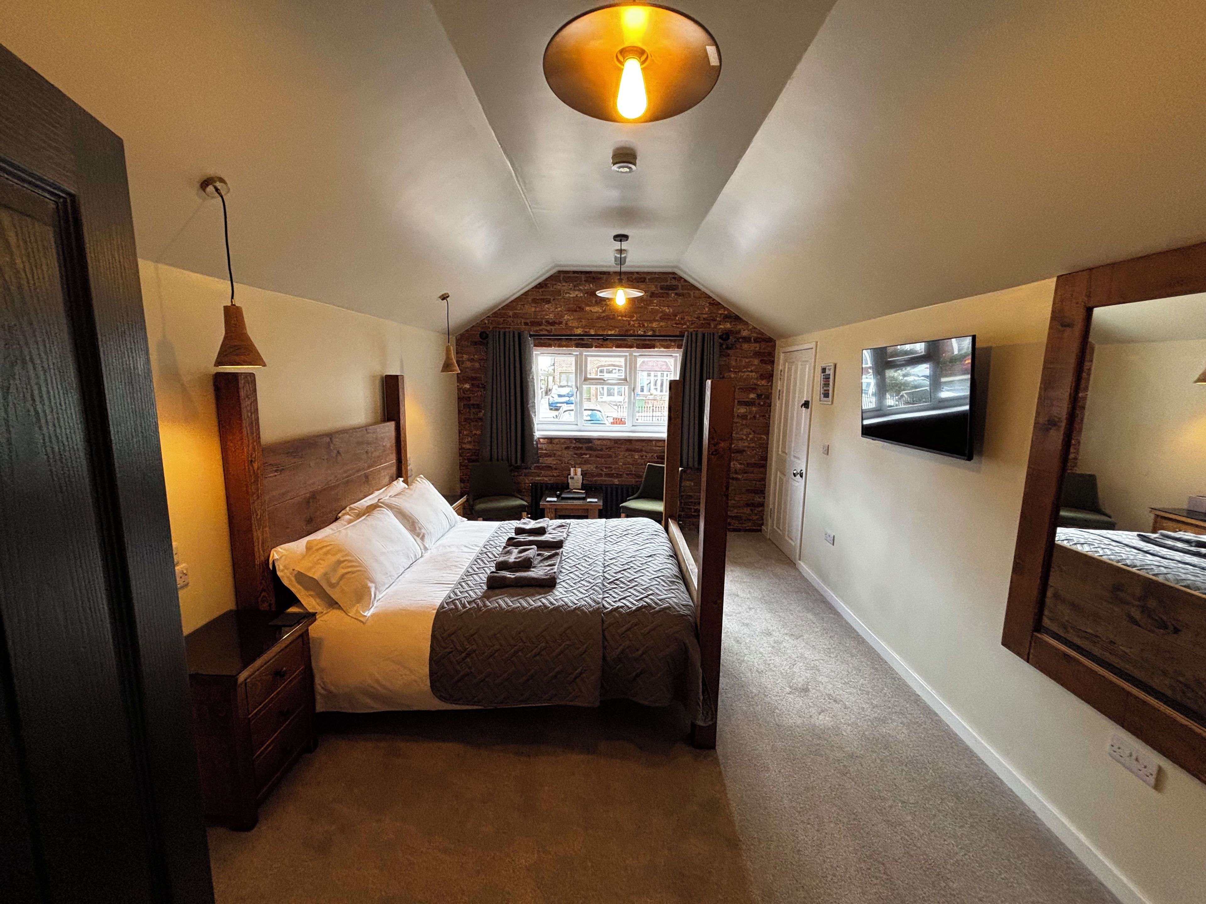A bedroom with a bed, a TV, a mirror, and a window with a view of the street.