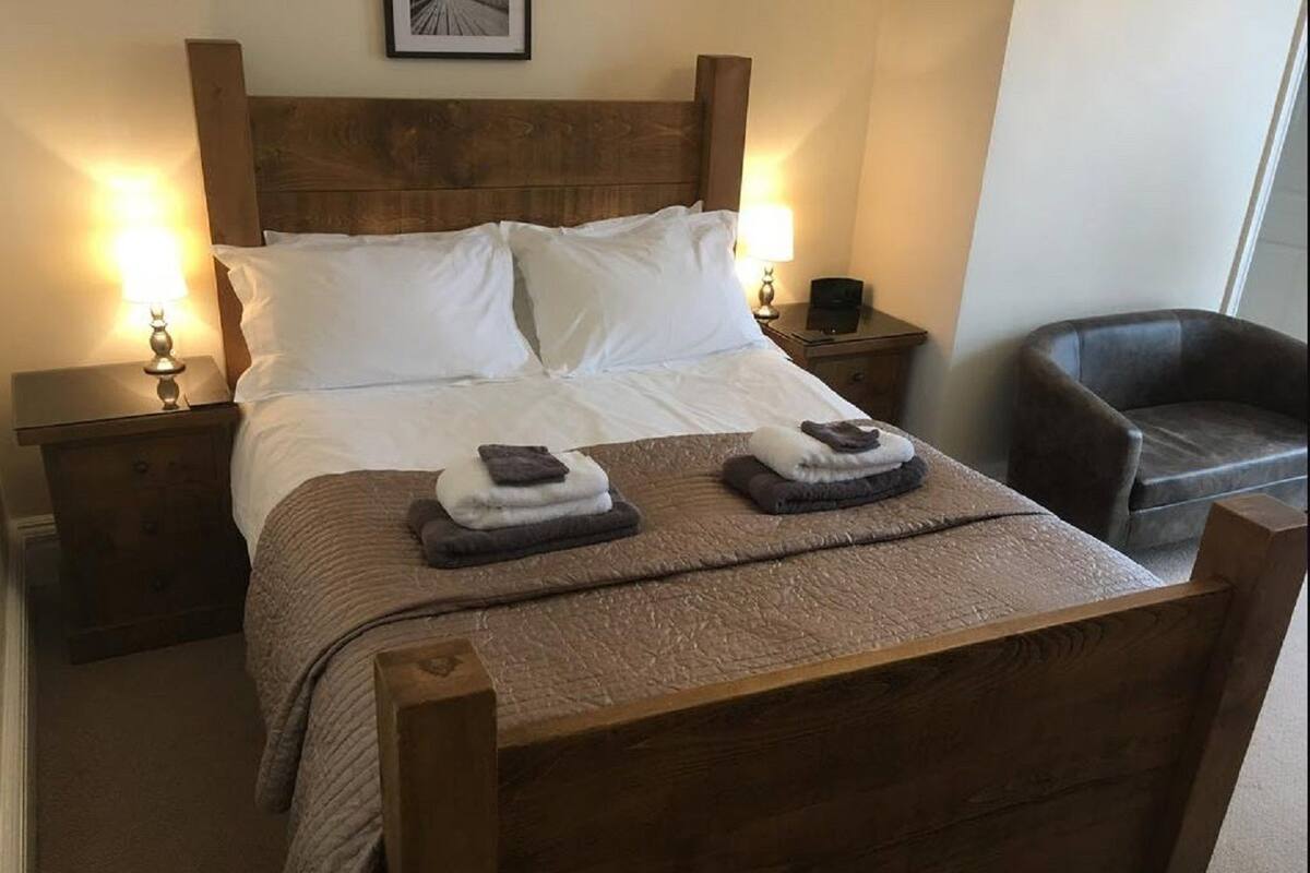 Una cama bien hecha con sábanas blancas, dos toallas dobladas y un cabecero de madera.