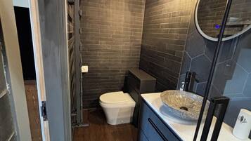 A modern bathroom with a stone sink, dark tiled walls, and a wooden floor.
