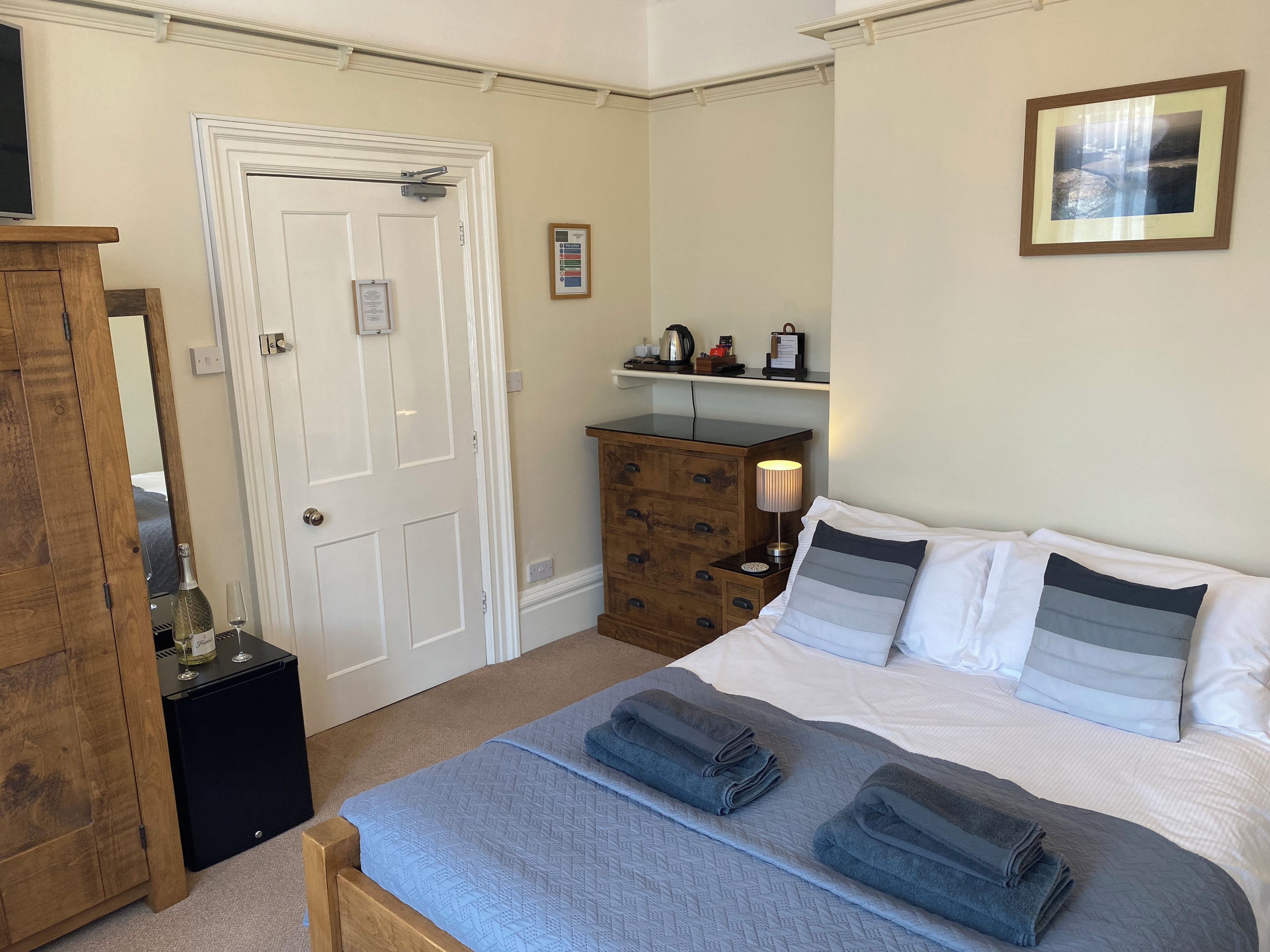 Una habitación de hotel con una cama, un aparador, un espejo, una puerta y una repisa con objetos encima.