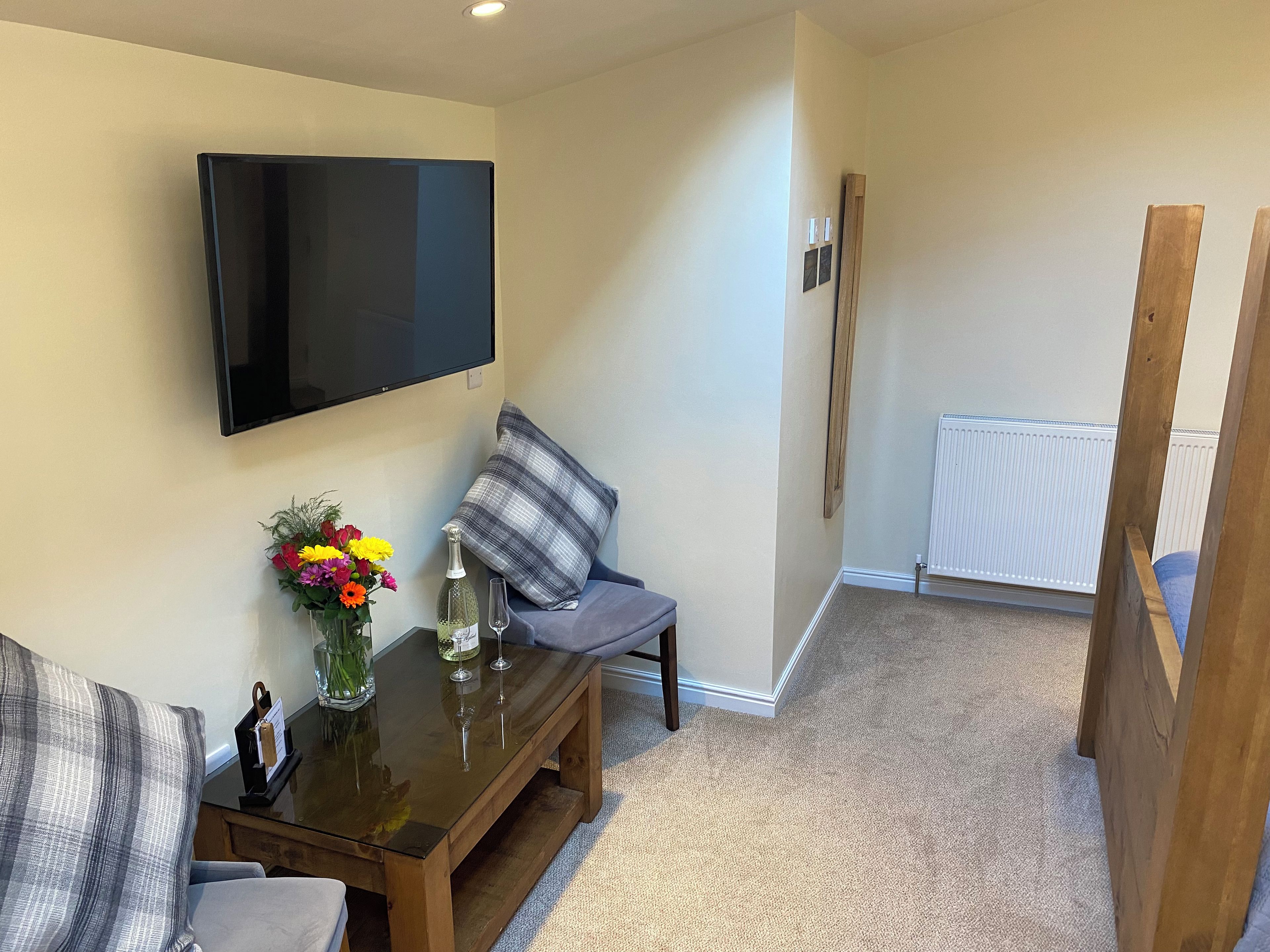 Una sala de estar con televisor de pantalla plana, una mesa de centro con un jarrón de flores, un sofá y un sillón gris.