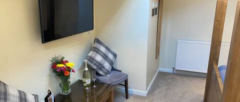 Un saló amb una televisió de pantalla plana, una taula de cafè amb un vas de flors, un sofà i un butaca gris.