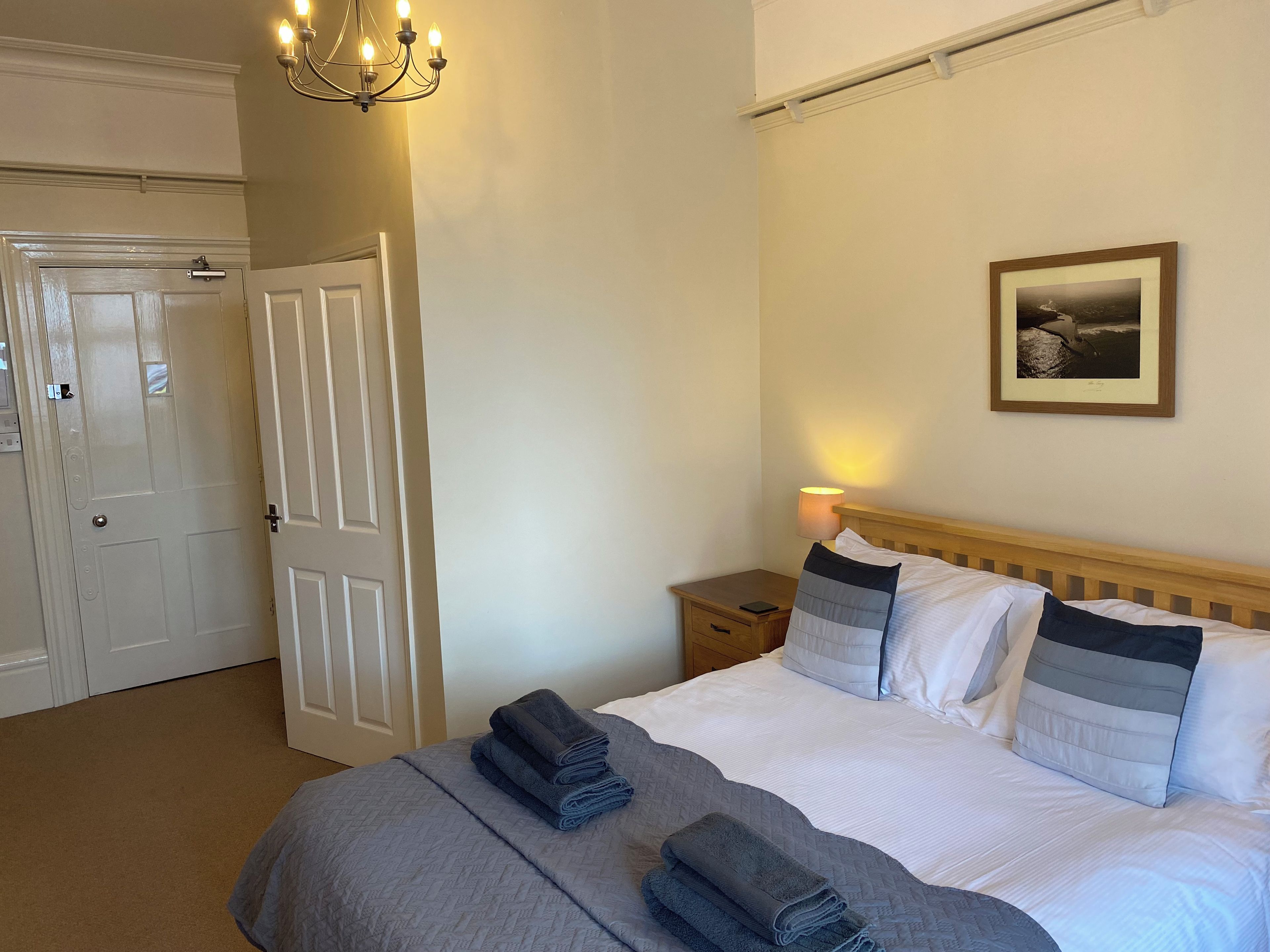 A hotel room with a bed, a bedside table, a lamp, a framed picture on the wall, and a door.