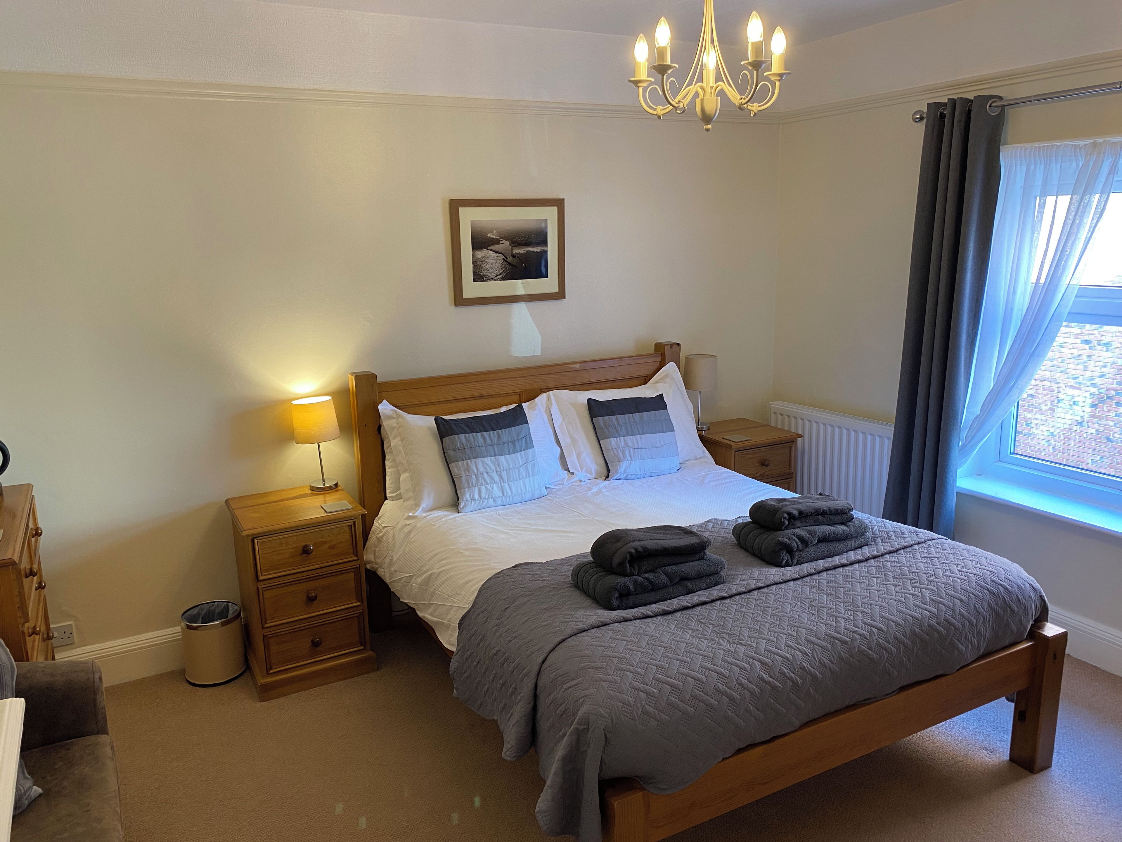 A neatly arranged bedroom with a wooden bed, bedside lamps, a radiator, and a window with curtains.