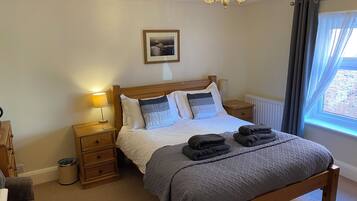 A neatly arranged bedroom with a wooden bed, bedside lamps, a radiator, and a window with curtains.