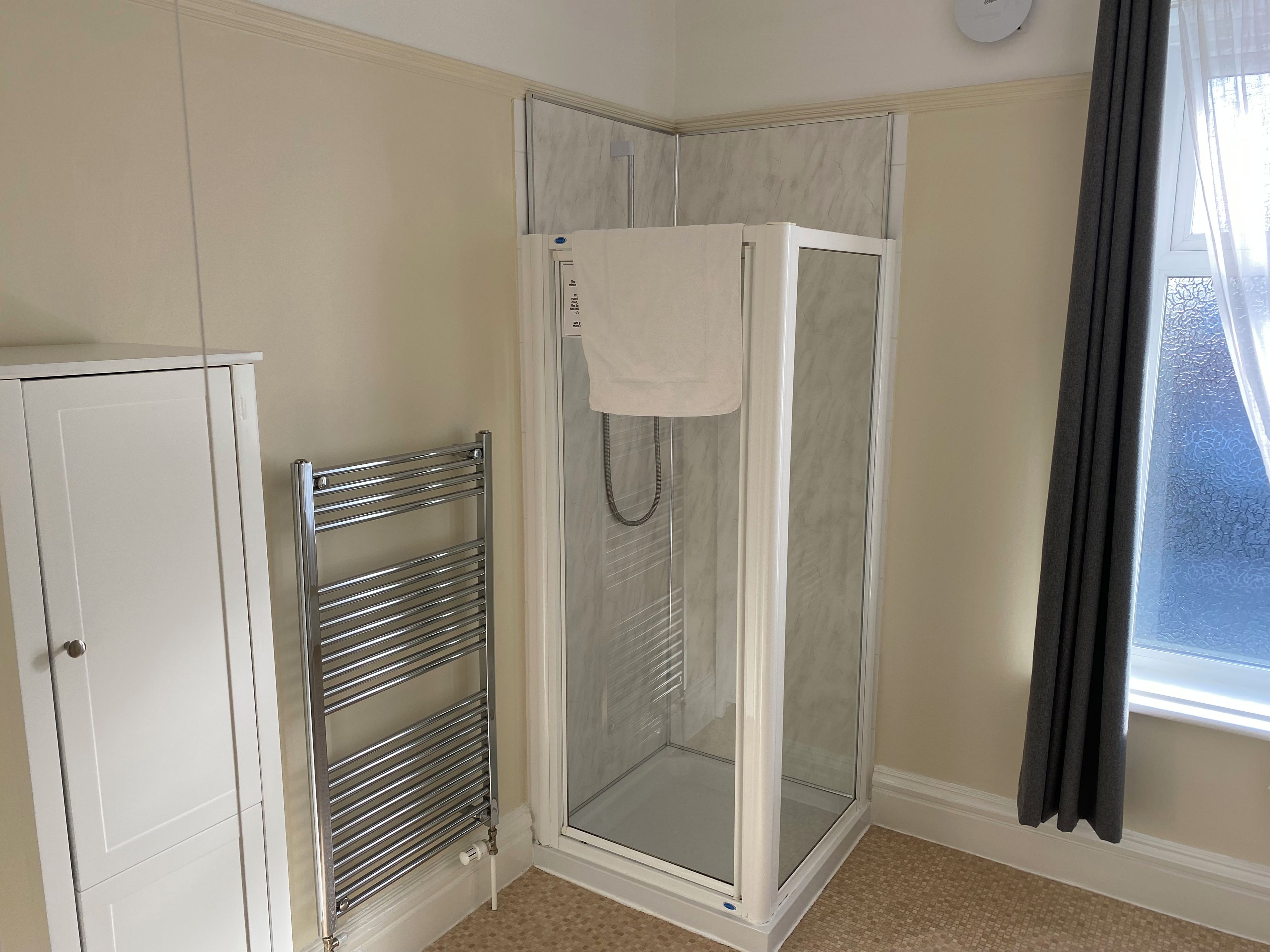 Un espace douche doté d’une porte en verre, une serviette accrochée à la porte et un porte-serviettes en métal.