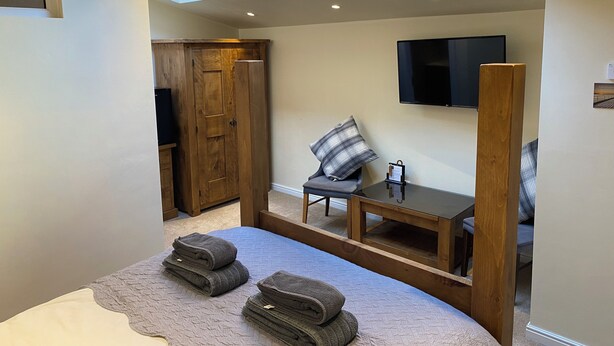 Een slaapkamer met dakramen, een bed, een televisie, een houten garderobe en een nachtkastje.