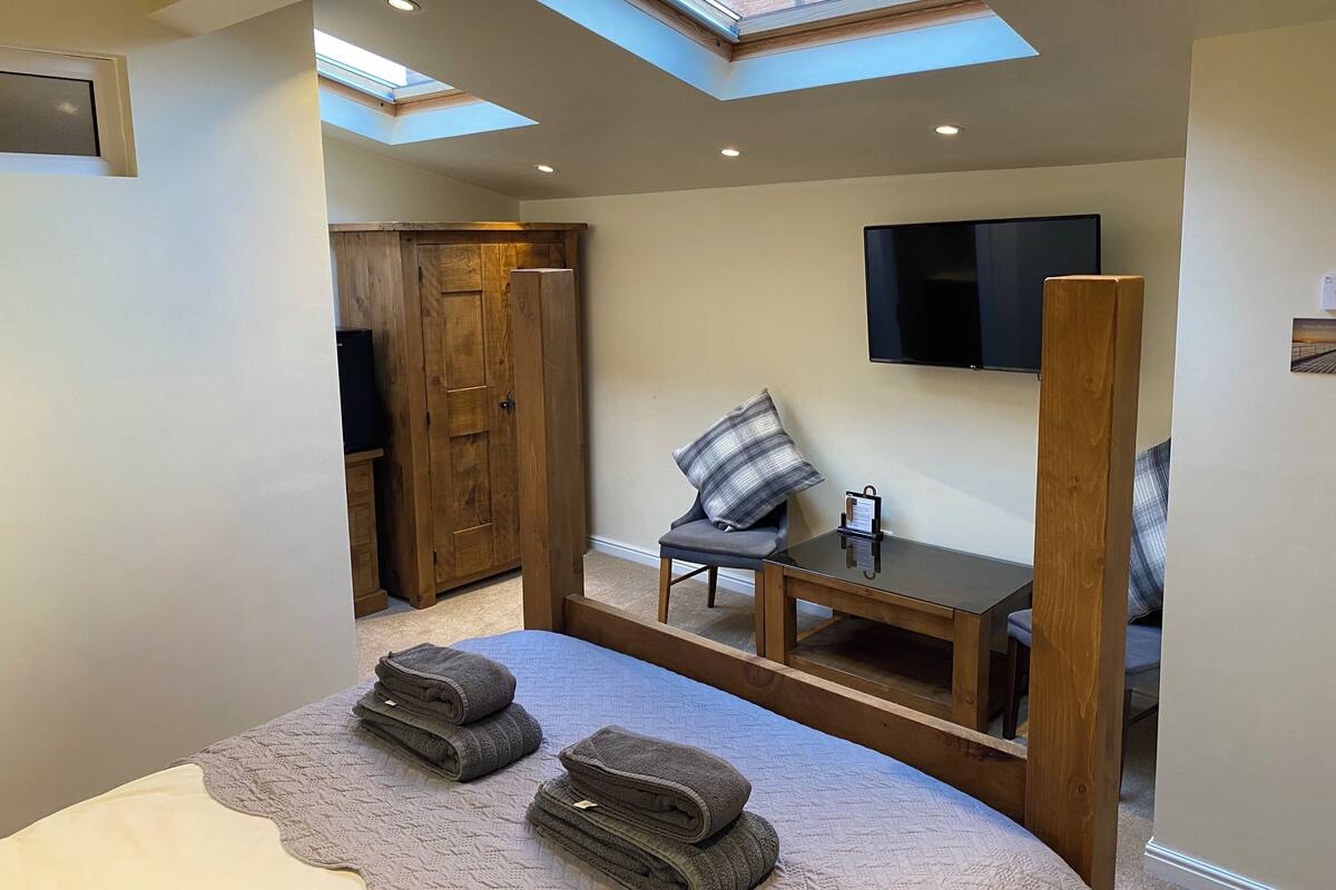 Un dormitorio con tragaluces, una cama, un televisor, un armario de madera y una mesita de noche.