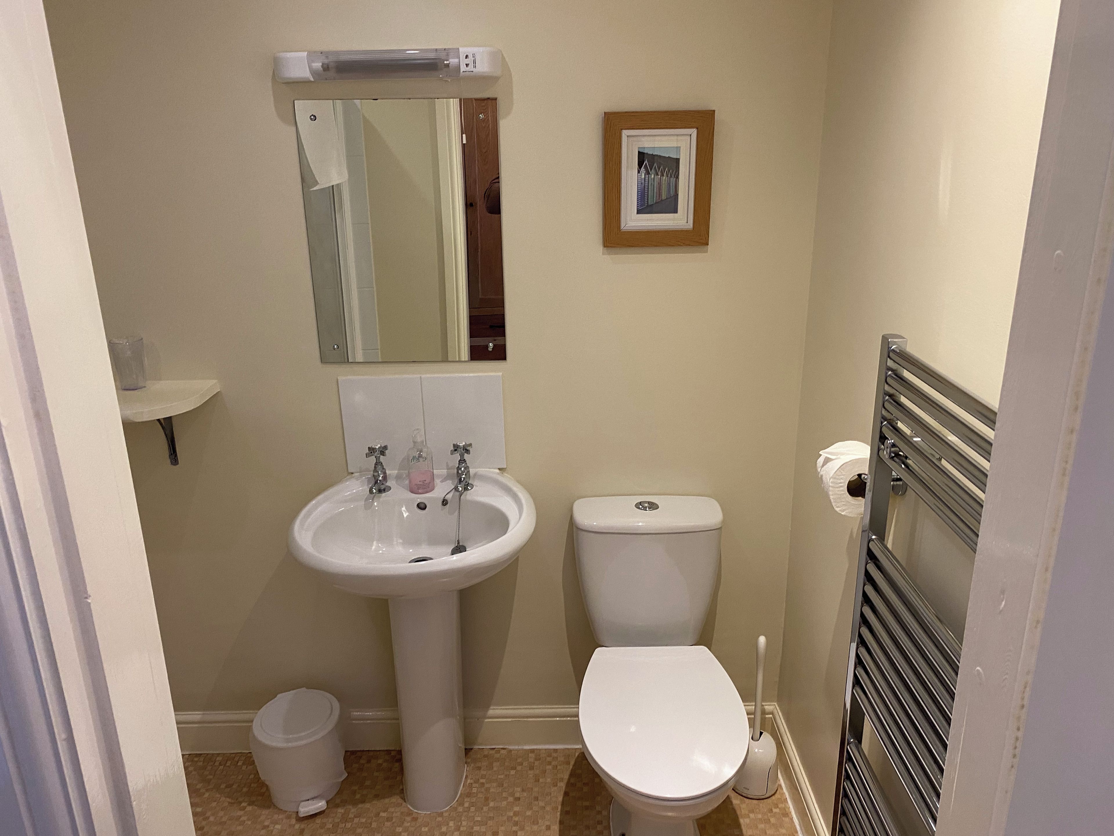 A bathroom with a sink, toilet, mirror, and a framed picture on the wall.