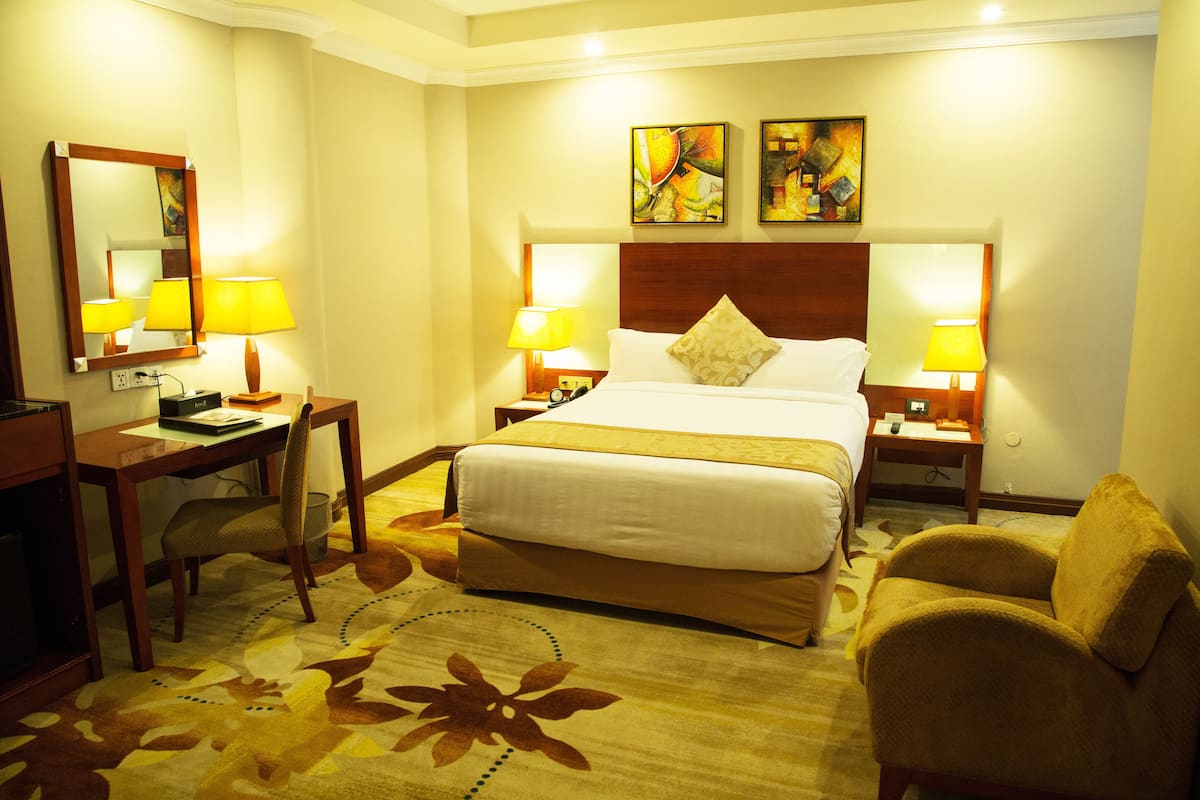 Une chambre d’hôtel avec un grand lit, deux tables de chevet avec des lampes, un bureau, une chaise et un sol recouvert d’une moquette.