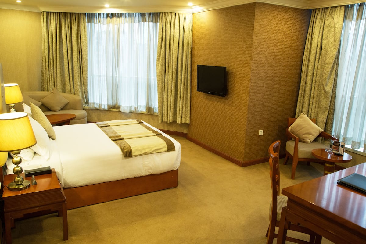 Une chambre d’hôtel avec un lit, un bureau, une chaise, une télévision et des rideaux.