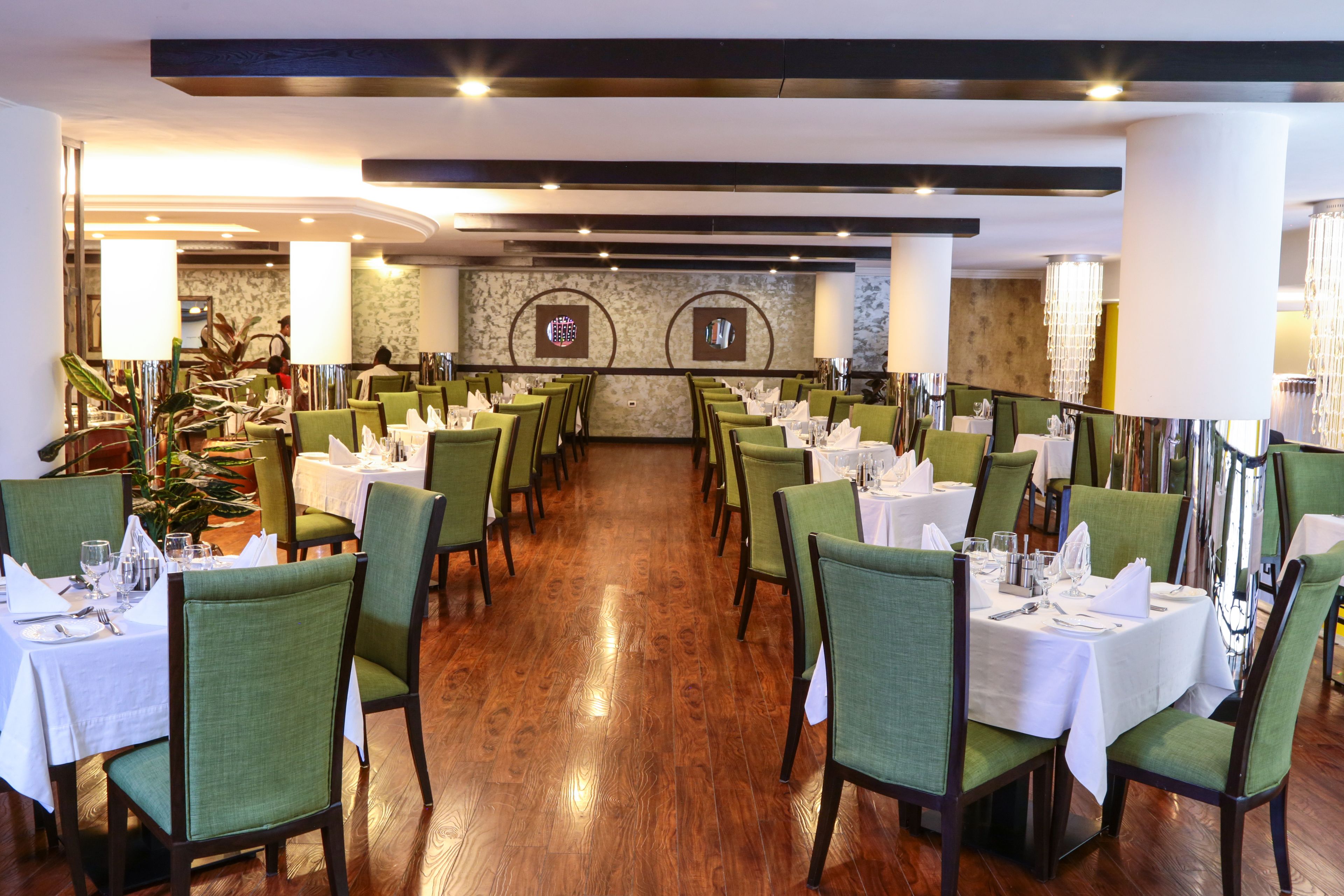 Un restaurante con sillas tapizadas de verde, manteles blancos y un piso de madera pulida.