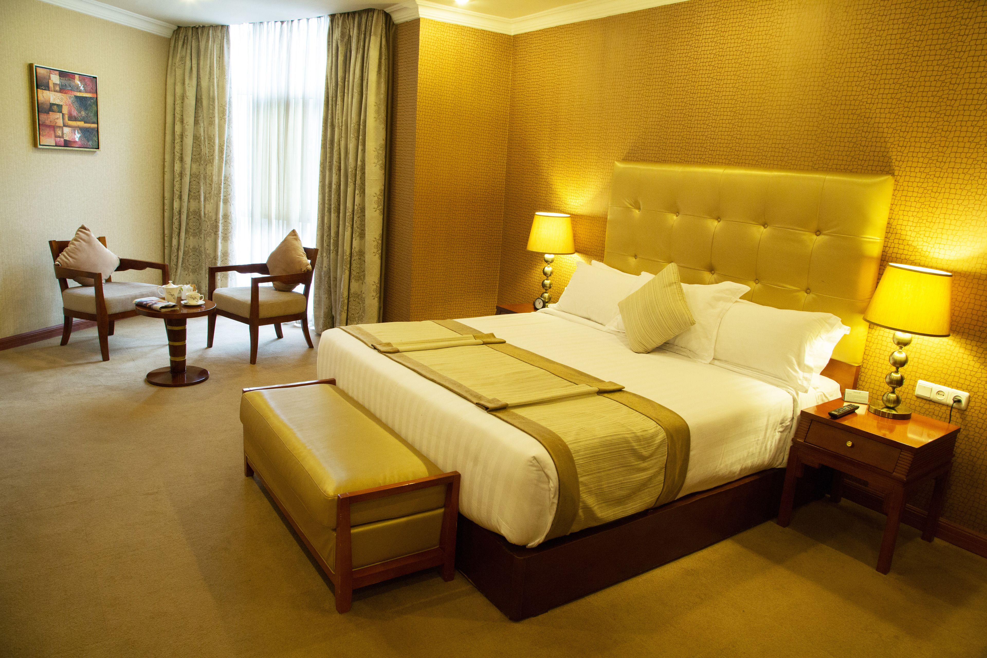 Una habitación de hotel con una cama grande, dos lámparas de noche, una mesita pequeña y dos sillas.