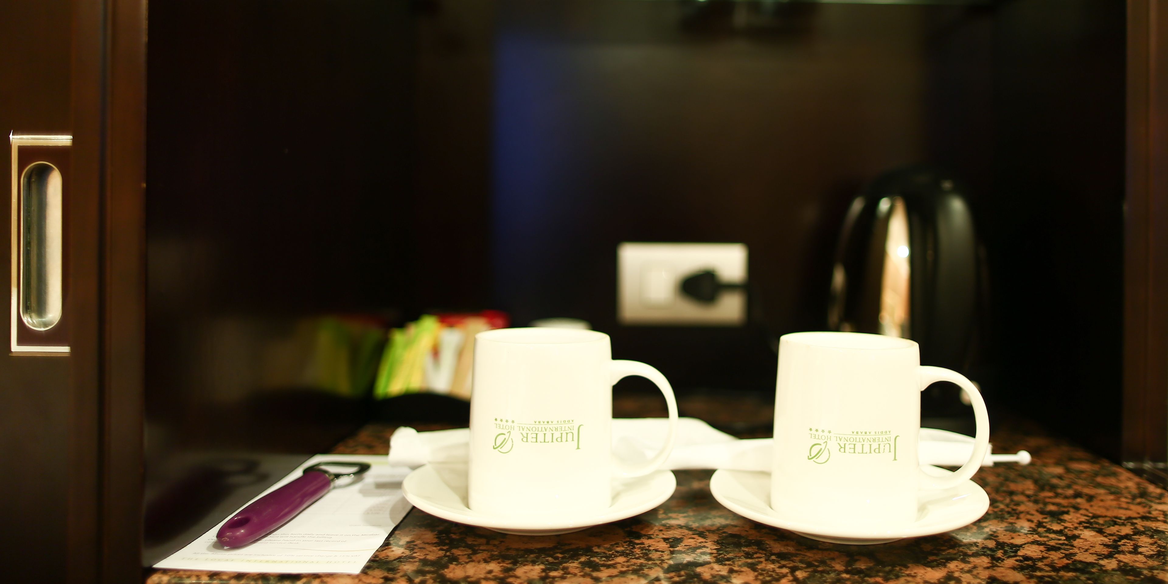 A kitchen counter with two white cups and a saucer, a purple pen, and a document.