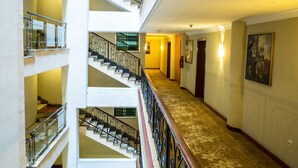 Un interior de varios niveles con una escalera central, un pasillo alfombrado y un cuadro en la pared.