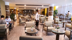 Un vestíbulo de hotel con varias zonas de estar, un bar y una recepción.