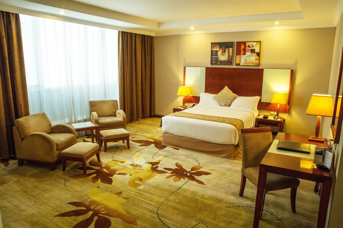 Une chambre d’hôtel avec un grand lit, deux tables de chevet avec des lampes, un bureau avec une chaise et un canapé.
